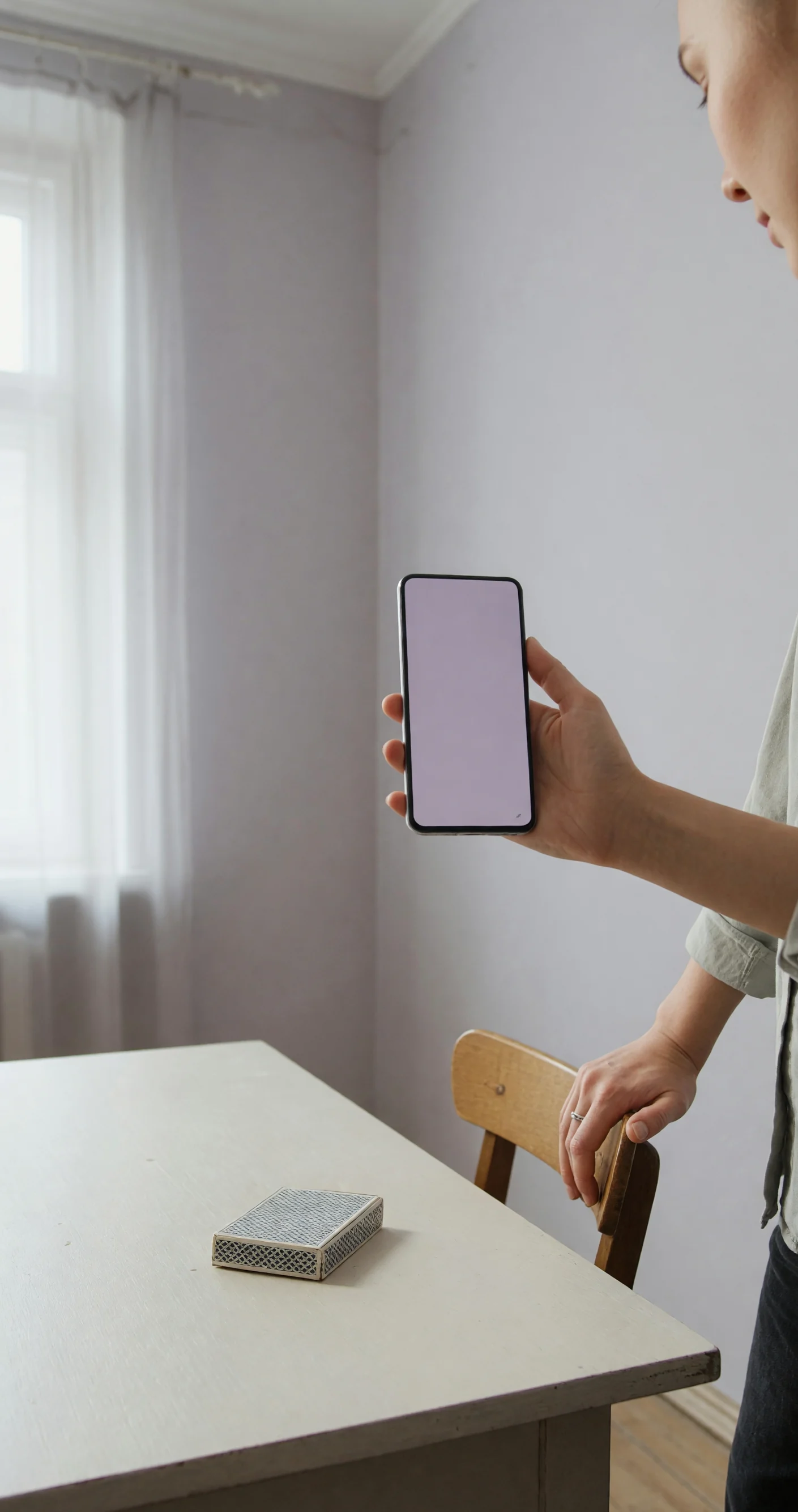 Adult holding a blank phone beside a chair and a face-down card packet