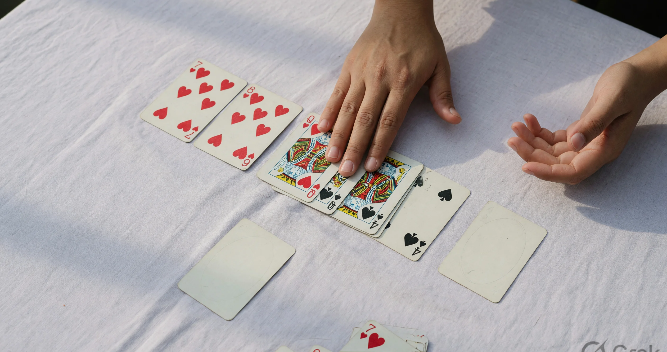 Declaration still Hand flattening a completed rummy layout onto ivory linen